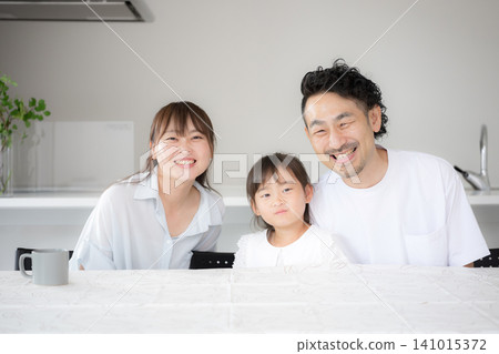A family portrait of a smiling family of three, showing their bright living room and their smiling faces looking directly at the camera. A family portrait of a smiling family of three, showing their bright living room and their smiling faces looking directly at the camera. 141015372