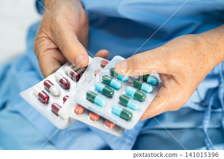 Asian senior woman patient holding antibiotics capsule pills in blister packaging. 141015396