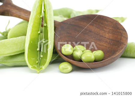 Fresh green peas spilling from a wooden spoon on a white background Fresh green peas spilling from a wooden spoon on a white background 141015800