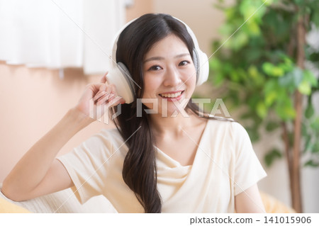 一位微笑的年輕女子戴著無線耳機欣賞音樂。 一位微笑的年輕女子戴著無線耳機欣賞音樂。 141015906