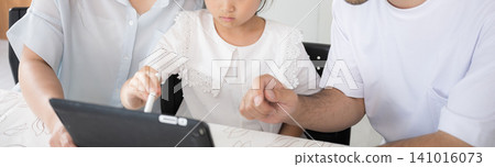 An image of a family of three (parents and two children) using a tablet for home learning, and digital education (faceless). An image of a family of three (parents and two children) using a tablet for home learning, and digital education (faceless). 141016073