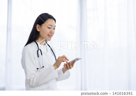 A Japanese female doctor operating her smartphone by the window. 141016391