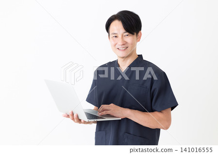 A middle-aged male doctor wearing navy blue scrubs and carrying a laptop. A middle-aged male doctor wearing navy blue scrubs and carrying a laptop. 141016555