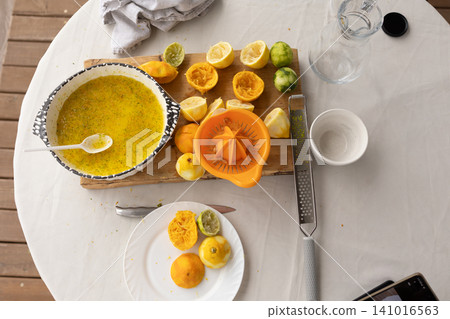 citrus juicing preparation on an outdoor table setting with a top-down view, creative and fresh approach to healthy lifestyle food preparation using wooden cutting board, ceramic bowl. citrus juicing preparation on an outdoor table setting with a top-down view, creative and fresh approach to healthy lifestyle food preparation using wooden cutting board, ceramic bowl. 141016563