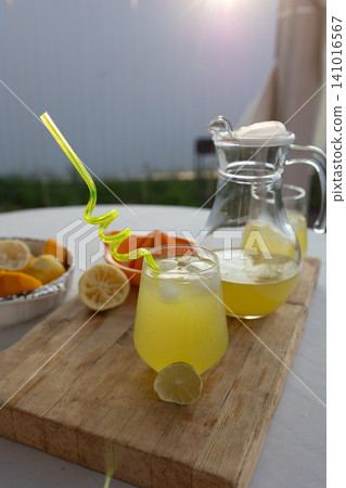 freshly served lemonade in glass with pitcher and lemons, ready to drink in outdoor setting with natural light, close-up, slightly elevated angle, vibrant yellow and green colors, mood: inv. 141016567