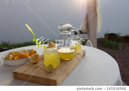 refreshing lemonade served on an outdoor patio with wooden board and ceramic bowl, close-up view of two glasses filled with lemonade and straws, vibrant yellow and green colors, summer time. 141016568