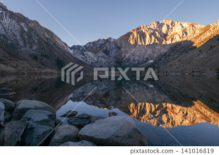 Serene sunrise over calm mountain lake with scenic reflection of majestic Sierra Nevada range. peaceful landscape captures tranquil beauty of nature Serene sunrise over calm mountain lake with scenic reflection of majestic Sierra Nevada range. peaceful landscape captures tranquil beauty of nature 141016819