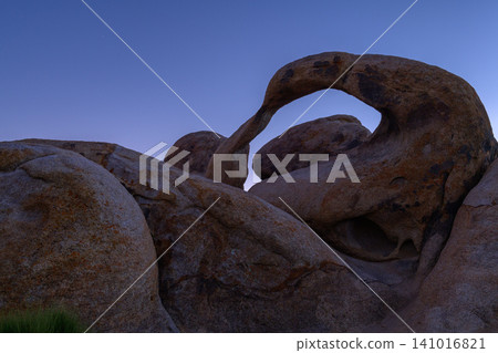 Serene arch rock formation against blue sky at dusk in sierra nevada desert landscape. natural stone monument appears peaceful and ancient under evening light Serene arch rock formation against blue sky at dusk in sierra nevada desert landscape. natural stone monument appears peaceful and ancient under evening light 141016821