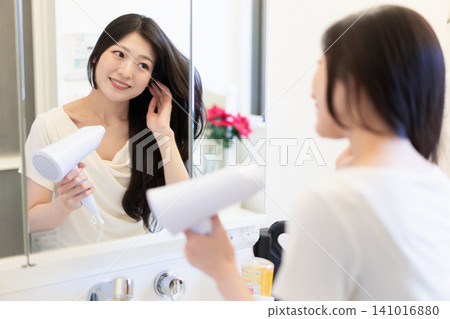 A young woman using a hairdryer at the bathroom sink. Beauty and hair care lifestyle. A young woman using a hairdryer at the bathroom sink. Beauty and hair care lifestyle. 141016880