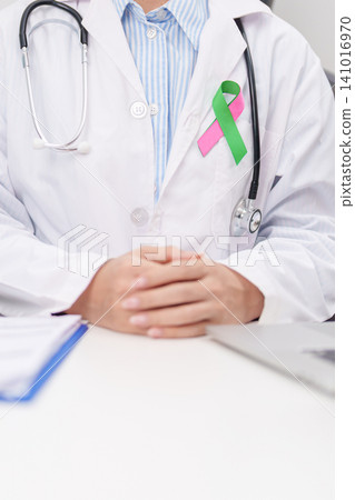 doctor using laptop and report notes on notebook. green and pink ribbon to patient for concept of October Metastatic Breast Cancer Awareness month, National Cancer Survivors Month and Pink October doctor using laptop and report notes on notebook. green and pink ribbon to patient for concept of October Metastatic Breast Cancer Awareness month, National Cancer Survivors Month and Pink October 141016970
