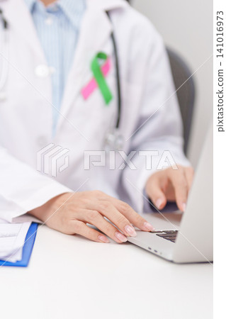 doctor using laptop and report notes on notebook. green and pink ribbon to patient for concept of October Metastatic Breast Cancer Awareness month, National Cancer Survivors Month and Pink October doctor using laptop and report notes on notebook. green and pink ribbon to patient for concept of October Metastatic Breast Cancer Awareness month, National Cancer Survivors Month and Pink October 141016973