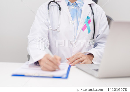 doctor using laptop and report notes on notebook. blue and pink ribbon concept of October male Breast Cancer Awareness month, National Cancer Survivors Month and Pink October Healthcare doctor using laptop and report notes on notebook. blue and pink ribbon concept of October male Breast Cancer Awareness month, National Cancer Survivors Month and Pink October Healthcare 141016978