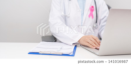 Professional doctor wearing lab coat using laptop and taking report notes on notebook for Breast Cancer Awareness month, World Cancer Day, National Cancer Survivors Month and Pink October in hospital Professional doctor wearing lab coat using laptop and taking report notes on notebook for Breast Cancer Awareness month, World Cancer Day, National Cancer Survivors Month and Pink October in hospital 141016987