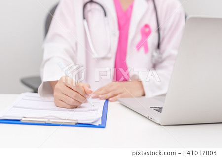 Professional doctor wearing lab coat using laptop and taking report notes on notebook for Breast Cancer Awareness month, World Cancer Day, National Cancer Survivors Month and Pink October in hospital Professional doctor wearing lab coat using laptop and taking report notes on notebook for Breast Cancer Awareness month, World Cancer Day, National Cancer Survivors Month and Pink October in hospital 141017003