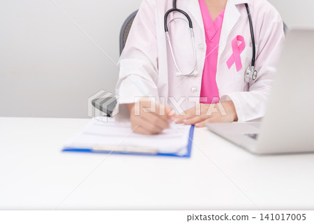 Professional doctor wearing lab coat using laptop and taking report notes on notebook for Breast Cancer Awareness month, World Cancer Day, National Cancer Survivors Month and Pink October in hospital Professional doctor wearing lab coat using laptop and taking report notes on notebook for Breast Cancer Awareness month, World Cancer Day, National Cancer Survivors Month and Pink October in hospital 141017005