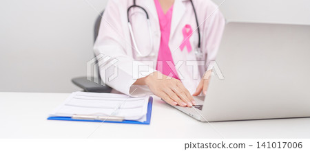 Professional doctor wearing lab coat using laptop and taking report notes on notebook for Breast Cancer Awareness month, World Cancer Day, National Cancer Survivors Month and Pink October in hospital Professional doctor wearing lab coat using laptop and taking report notes on notebook for Breast Cancer Awareness month, World Cancer Day, National Cancer Survivors Month and Pink October in hospital 141017006