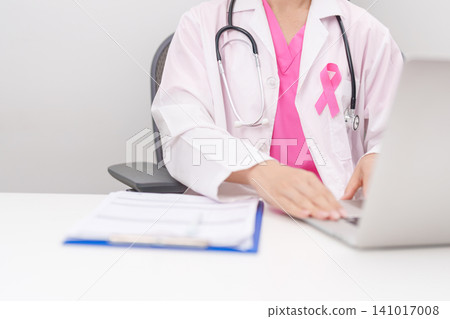 Professional doctor wearing lab coat using laptop and taking report notes on notebook for Breast Cancer Awareness month, World Cancer Day, National Cancer Survivors Month and Pink October in hospital Professional doctor wearing lab coat using laptop and taking report notes on notebook for Breast Cancer Awareness month, World Cancer Day, National Cancer Survivors Month and Pink October in hospital 141017008