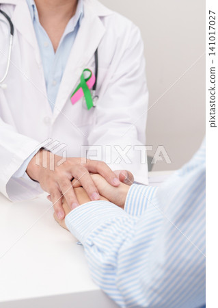 doctor hold patient hand to comfort and support with empathy. green and pink ribbon to patient for concept of October Metastatic Breast Cancer Awareness month, National Cancer Survivors Month doctor hold patient hand to comfort and support with empathy. green and pink ribbon to patient for concept of October Metastatic Breast Cancer Awareness month, National Cancer Survivors Month 141017027