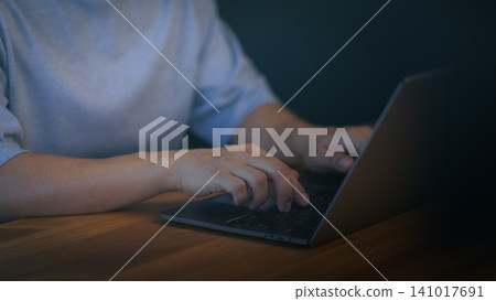 Person working on laptop computer in room, representing remote work, online communication, digital productivity, technology usage, freelance business and modern workspace. 141017691