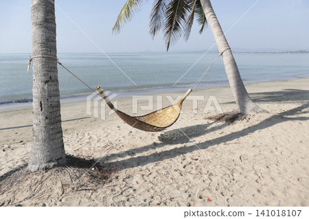 A bamboo hammock hangs under a coconut tree on the beach by the sea. A bamboo hammock hangs under a coconut tree on the beach by the sea. 141018107