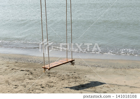 A wooden hanging swing on the beach by the sea. A wooden hanging swing on the beach by the sea. 141018108