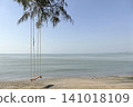A wooden swing hanging under a pine tree on the beach by the sea. 141018109