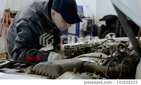 Skilled mechanic examining car engine, wearing protective gloves and performing diagnostic checks in professional workshop environment 141018315