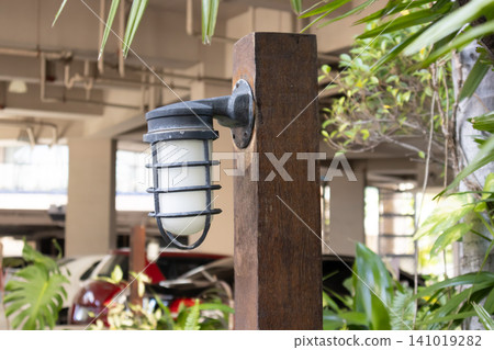 Wooden post wall lamp outdoor light garden light caged lamp metal fixture lamp shade electric light illumination rustic vertical post brown wood black metal white glass exterior patio porch Wooden post wall lamp outdoor light garden light caged lamp metal fixture lamp shade electric light illumination rustic vertical post brown wood black metal white glass exterior patio porch 141019282