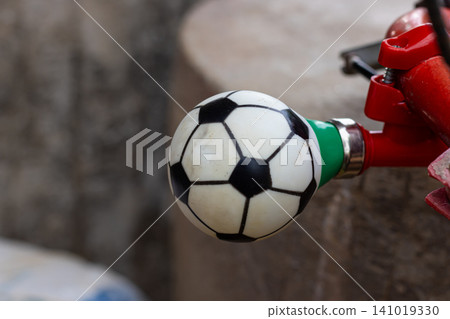 Soccer ball on red clamp with green connector against blurred stone background in close up outdoor detail Soccer ball on red clamp with green connector against blurred stone background in close up outdoor detail 141019330