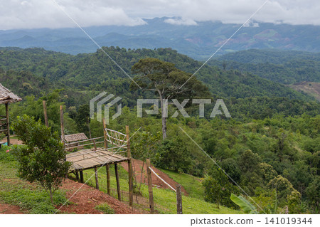 Mountain landscape with lush forest and cloudy sky, wooden platform overlook on green hillside Mountain landscape with lush forest and cloudy sky, wooden platform overlook on green hillside 141019344