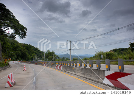 Empty highway curve concrete road barrier overcast sky mountain view tropical forest rural road empty road traffic safety road construction travel route asphalt lane guard rail warning sign Empty highway curve concrete road barrier overcast sky mountain view tropical forest rural road empty road traffic safety road construction travel route asphalt lane guard rail warning sign 141019349