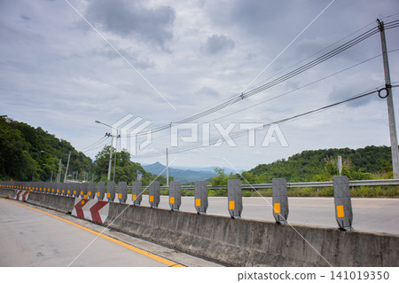 Road barrier mountain road cloudy sky empty highway guard rail power line rural landscape concrete barrier curve road green hill Road barrier mountain road cloudy sky empty highway guard rail power line rural landscape concrete barrier curve road green hill 141019350