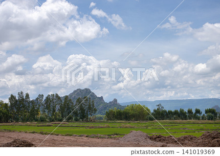 Cloudy sky green field mountain range rural landscape tree line dirt road grass field blue sky scenic view open land Cloudy sky green field mountain range rural landscape tree line dirt road grass field blue sky scenic view open land 141019369