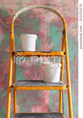 Step ladder with two white paint buckets standing in front of decorative textured wall during interior renovation. Home painting equipment for DIY, remodeling, and home improvement concepts 141019379