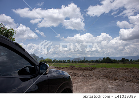 Car side view rural road cloudy sky landscape field mountain dirt road black vehicle countryside horizon Car side view rural road cloudy sky landscape field mountain dirt road black vehicle countryside horizon 141019389