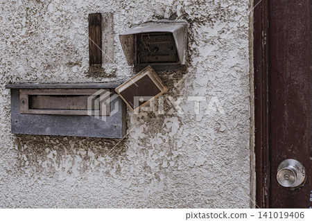 A broken intercom and a weathered mailbox. 141019406