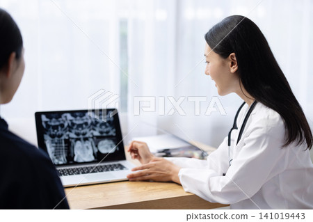 A young Japanese female doctor explains X-ray images displayed on her laptop to a patient. A young Japanese female doctor explains X-ray images displayed on her laptop to a patient. 141019443