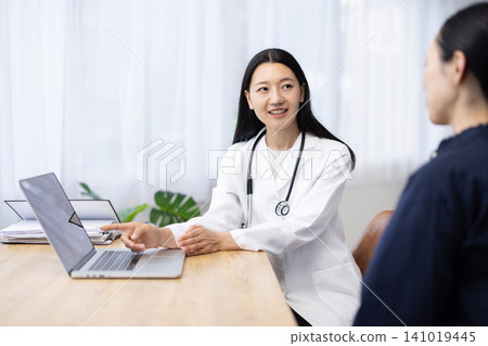 A young Japanese female doctor explains X-ray images displayed on her laptop to a patient. A young Japanese female doctor explains X-ray images displayed on her laptop to a patient. 141019445