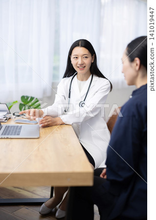 A young Japanese female doctor explains X-ray images displayed on her laptop to a patient. 141019447