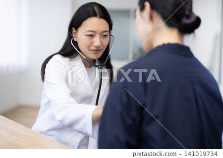 A young Japanese female doctor using a stethoscope during an examination. 141019734