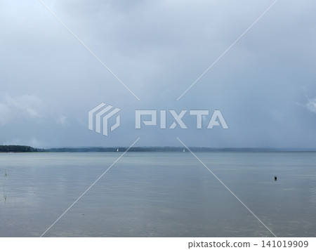 Misty lake landscape with distant sailboats under gray overcast sky Misty lake landscape with distant sailboats under gray overcast sky 141019909