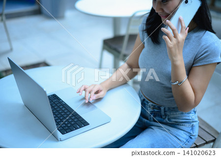 Closeup business woman working on a laptop and using smartphone sitting on at outdoor cafe workspace 141020623