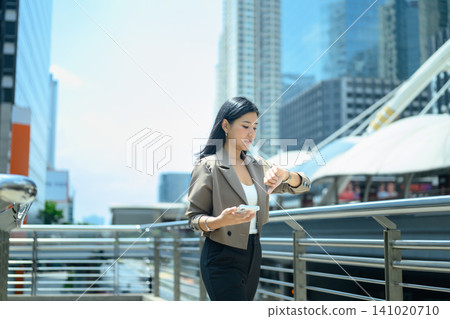 Businesswoman checks smartwatch while walking in modern city Businesswoman checks smartwatch while walking in modern city 141020710