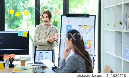 Young Asian Gen Z Female Developer Presenting Mobile App UI UX Design to Colleague in Modern Office Young Asian Gen Z Female Developer Presenting Mobile App UI UX Design to Colleague in Modern Office 141020728