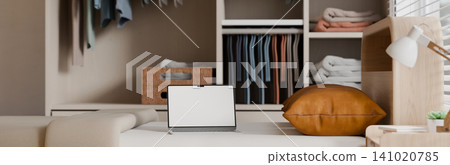Laptop with Blank White Screen Mockup on Sofa in Cozy Bedroom with Organized Wardrobe Closet Laptop with Blank White Screen Mockup on Sofa in Cozy Bedroom with Organized Wardrobe Closet 141020785