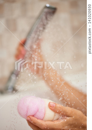 Hands holding a pink body sponge under splashing water, highlighting hygiene, daily routine, and personal care Hands holding a pink body sponge under splashing water, highlighting hygiene, daily routine, and personal care 141020930