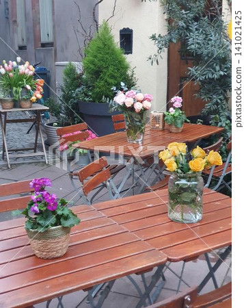 Outdoor Cafe Tables With Fresh Flower Arrangements On Wooden Bistro Tables In Charming Courtyard Outdoor Cafe Tables With Fresh Flower Arrangements On Wooden Bistro Tables In Charming Courtyard 141021425