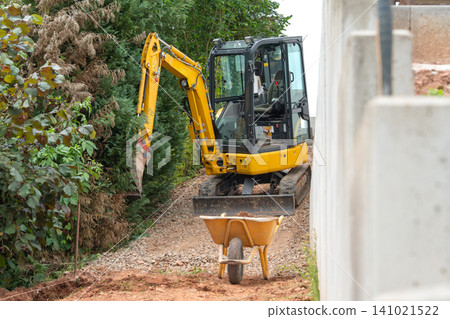 mini excavator at work near greenery on construction site, concrete blocks and soil in wheelbarrow, industrial scene, side view, vivid yellow and green tones, clean and detailed industrial. mini excavator at work near greenery on construction site, concrete blocks and soil in wheelbarrow, industrial scene, side view, vivid yellow and green tones, clean and detailed industrial. 141021522