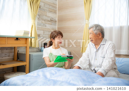 A care worker conducts a medical interview at the patient's bedside. A care worker conducts a medical interview at the patient's bedside. 141021610