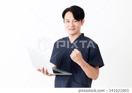 一位身穿藏藍色手術服的中年男醫師手持筆記型電腦,做出勝利的手勢。 一位身穿藏藍色手術服的中年男醫師手持筆記型電腦,做出勝利的手勢。 141021803